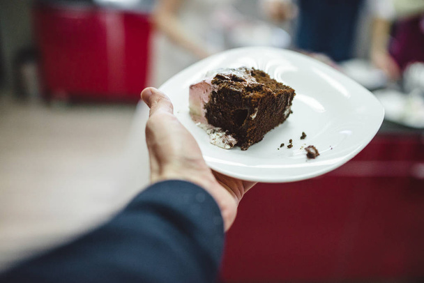 mens hand holding Slice of glazed chocolate wedding cake on the plate - Foto, afbeelding