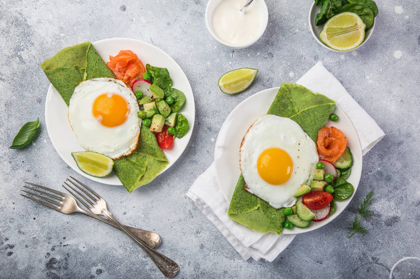 green spinach crepes with fried eggs, smoked salmon and vegetables for breakfast, top view - Photo, Image