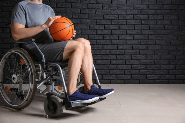 Young basketball player sitting in wheelchair against dark brick wall - Foto, afbeelding