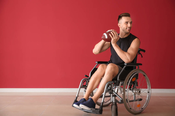 Nuori mies rugby pallo istuu pyörätuolissa vastaan väriseinä
 - Valokuva, kuva