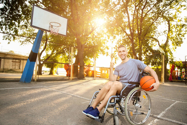 Молодой человек с мячом сидит в инвалидной коляске на открытом воздухе
 - Фото, изображение