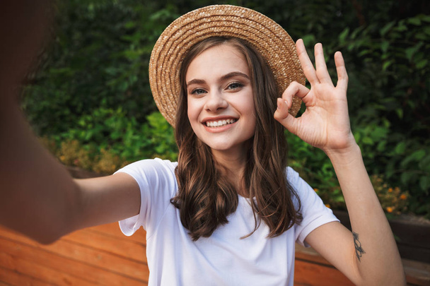 Smiling young girl taking a selfie with outsretched hand at the park outdoors, showing ok - Foto, immagini