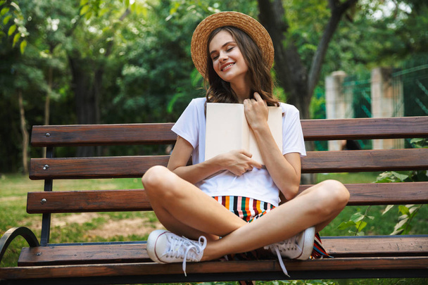 Χαρά κοπέλα διαβάζοντας ένα βιβλίο, ενώ κάθεται στο πάρκο σε εξωτερικούς χώρους - Φωτογραφία, εικόνα