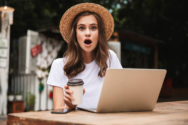 Innoissaan nuori tyttö juo kahvia istuessaan kannettavan tietokoneen kanssa kahvilassa ulkona
 - Valokuva, kuva