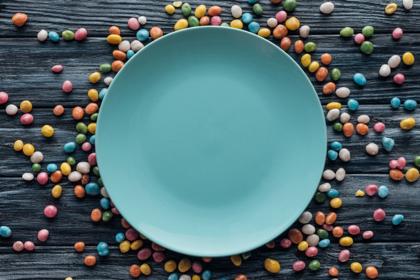 vista superior del plato vacío rodeado de caramelos de colores en la mesa de madera
  - Foto, Imagen