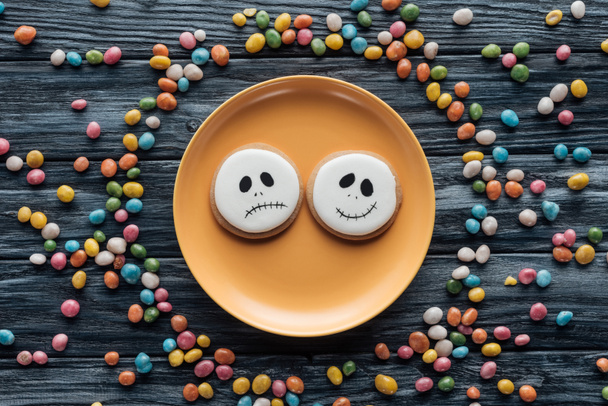 Draufsicht auf Teller mit Halloween-Plätzchen umgeben von bunten Bonbons auf Holztisch  - Foto, Bild