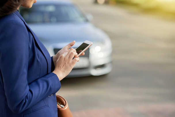 αγνώριστος επιχειρηματίας φορώντας κλασική Μπουφάν χρησιμοποιώντας smartphone ενώ στέκεται στην άκρη του δρόμου - Φωτογραφία, εικόνα