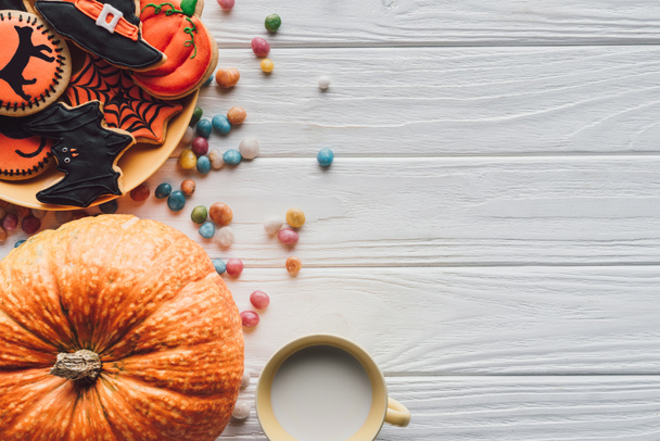 vista elevada de abóbora, prato com biscoitos de Halloween, doces e xícara com leite no fundo de madeira
  - Foto, Imagem
