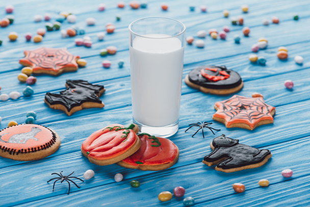 close up view of candies, homemade halloween cookies and glass of milk on wooden table  - Photo, Image