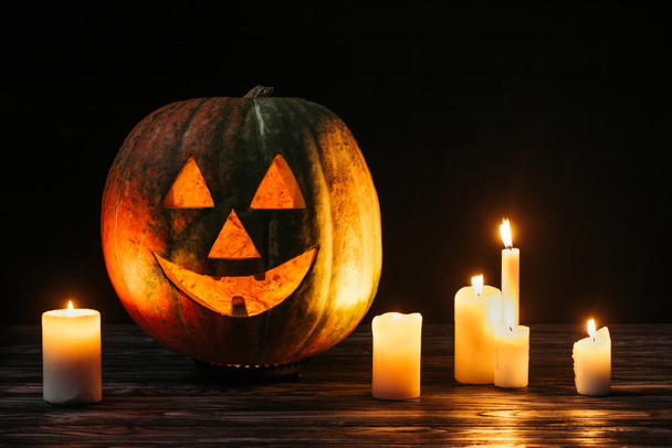 scary jack o lantern with candles on wooden table on black background - Photo, Image