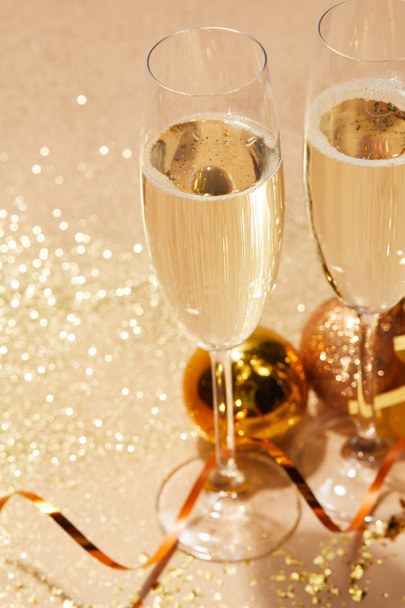 close up of  two glasses of champagne and christmas toys with glitter on tabletop - Fotoğraf, Görsel