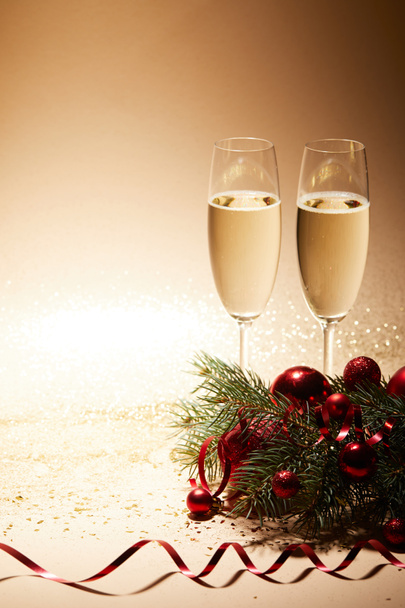 twee glazen voor champagne, rood glanzend kerstballen en pine tak op glinsterende tafelblad - Foto, afbeelding