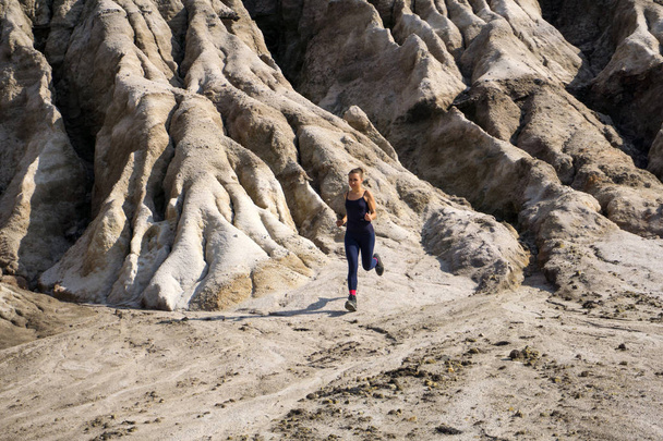 slanke sportieve meisje loopt langs een ruwe, verlaten bergachtig terrein - Foto, afbeelding
