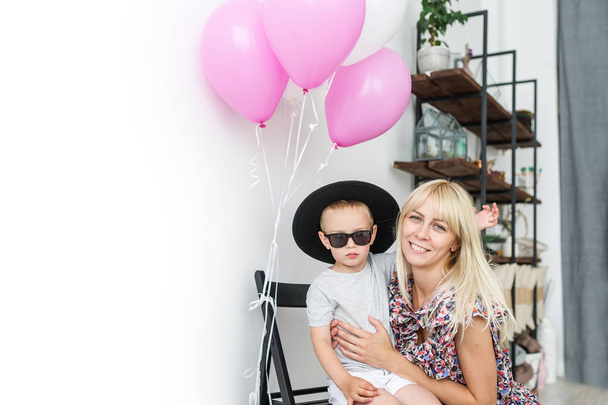 Portrait d'un petit garçon heureux avec sa mère sur fond de ballons roses. Maman et fils jouent anniversaire de vacances
.  - Photo, image