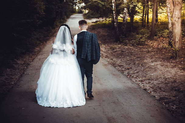 beautiful bride and groom in wedding dresses on a wedding walk go into the distance - Foto, Imagen