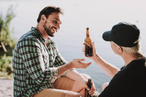 Smiling Men Drinking Beer near River in Summer. Man in Shirt. Bearded Guy. Weekend on River. Young Man. Relaxing Outdoor. Sitting Man. Man near Lake. Drinking Alkohol. Beer in Bottle. - Foto, immagini