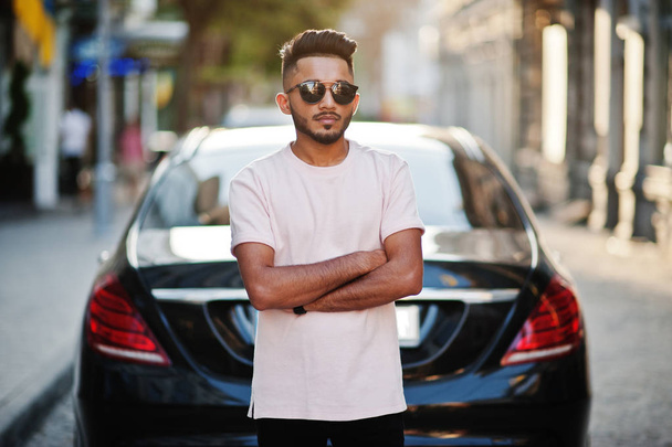 Stylish indian beard man at sunglasses and pink t-shirt against luxury car. India rich model posed outdoor at streets of city. - Φωτογραφία, εικόνα