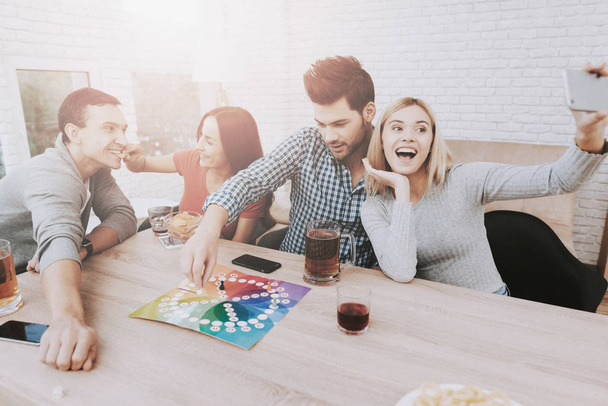 Young Smiling People Have Fun on Party at Home. Playing Games. Eating Snacks. Indoor Fun. Young Smiling Girl. Young Smiling Guy. Sitting at Table. Party with Friends. Indoor Activities Concept. - Φωτογραφία, εικόνα