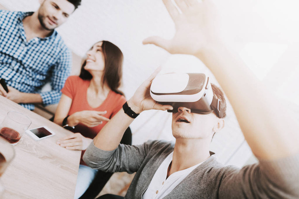 Young Smiling People Have Fun with Virtual Reality Device on Party at Home. Indoor Fun. Young Smiling Girl. Young Smiling Guy. Sitting at Table. Party with Friends. Indoor Activities Concept. - 写真・画像
