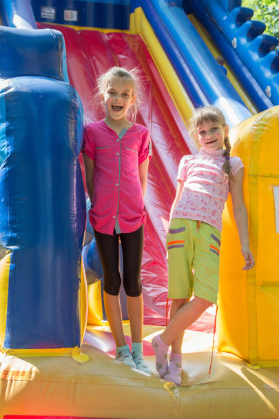 Duas meninas alegres estão na entrada de um grande trampolim inflável
 - Foto, Imagem