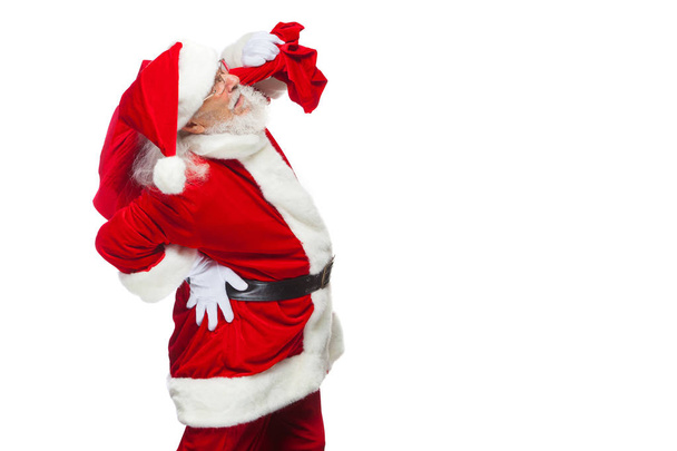 Christmas. Santa Claus is suffering from back pain and holds a red bag with gifts on his back. Isolated on white background. - Photo, image
