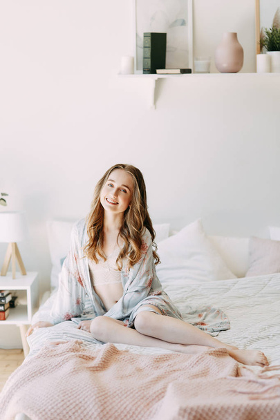 Girl in the early morning in bed and Bathrobe, wakes up and getting ready to work. Productive day. Smiles and laughs. Lying in bed, catching the sunrise. Happy morning in the bedroom. - Foto, imagen