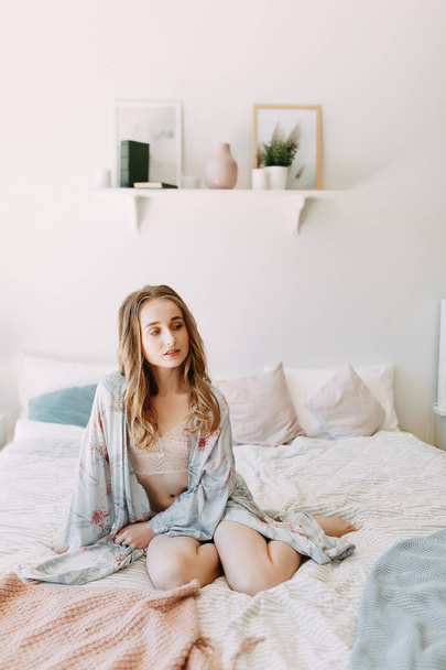 Girl in the early morning in bed and Bathrobe, wakes up and getting ready to work. Productive day. Smiles and laughs. Lying in bed, catching the sunrise. Happy morning in the bedroom. - Foto, Imagem