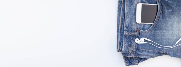 Long wide banner Flat lay of blue jeans and smartphone headphones isolated on white background with copy space. Overhead view of woman casual outfit. Trendy hipster look top view - Photo, Image