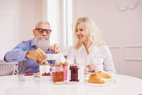 Happy senior couple having breakfast at home - Married couple on the 60's in their apartment, concepts about senority and relationship - 写真・画像