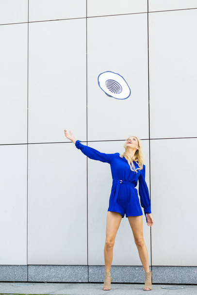 Happy joyful woman wearing blue jumpsuit having fun throwing her sun hat. Fashion model and summer outfit. - Photo, image