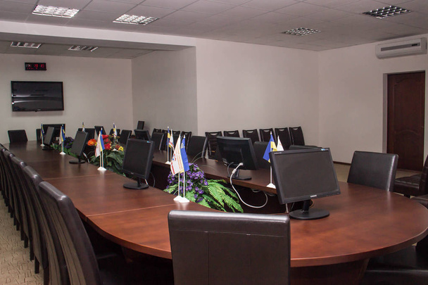 Mesa ovalada de madera natural con asientos de cuero en la sala de conferencias con banderas de Ucrania
 - Foto, Imagen