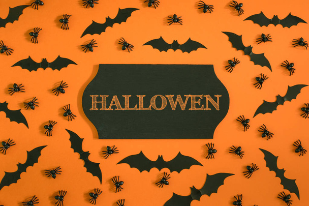 In the center of the orange background is an empty black plaque with the inscription Halloween. Around the spiders and the Halloween bats. Beautiful picture from the top. - Foto, imagen
