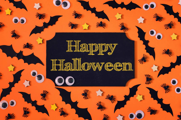 A közepén a narancssárga háttér a felirat a Happy Halloween jele. Körül, kis díszítő denevérek, a pókok és a báb szemek. Egy szép elrendezés a Halloween. - Fotó, kép