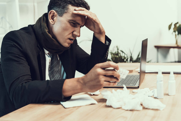 Sick Man in Suit with Scarf Sitting in Office. Manager in Modern Office. Healthcare Concept. Modern Office. Sick Worker. Healthcare in Office. Wooden Table. Digital Device. Laptop on Desk. - Photo, Image