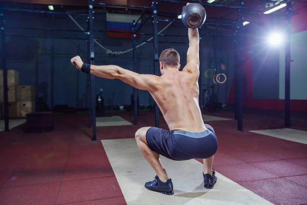 Cross training fit. Fitness man doing a weight training by lifting kettlebell. Young athlete doing kettlebell swings. Bodybuilder lifting kettlebell. Cross instructor fit at the gym. Cross in the gym - Photo, image