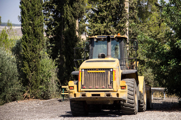 Egy narancssárga traktor áll, az árnyék a bokrok és fák, megelőlegezve a vetési szezonban. - Fotó, kép
