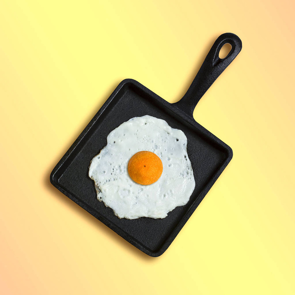 Square cast-iron frying pan with fried eggs, half orange instead of yolk. Artificial objects that mimic natural forms. Creative idea, imagination and fantasy. Original minimal concept - Photo, Image