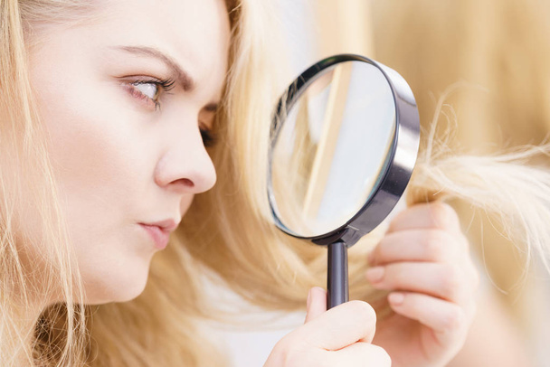 Split ends problem, dry effect, haircare concept. Unhappy blonde woman looking at destroyed damaged hair through magnifying glass - Fotografie, Obrázek