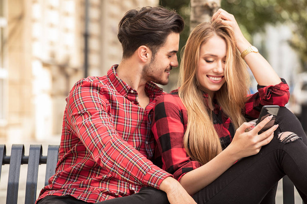 Smiling couple in love dating outdoors.Young happy couple sitting, looking at mobile phone. - Foto, Imagen