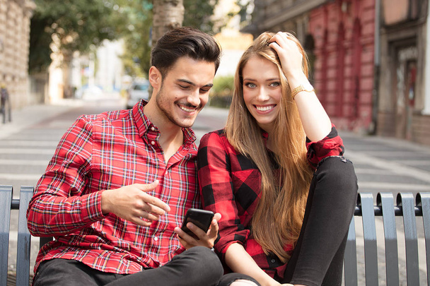 Smiling couple in love dating outdoors.Young happy couple sitting, looking at mobile phone. - Foto, imagen