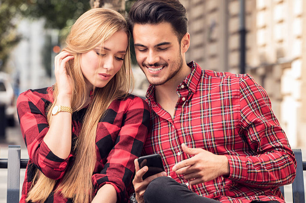 Smiling couple in love dating outdoors.Young happy couple sitting, looking at mobile phone. - Photo, Image