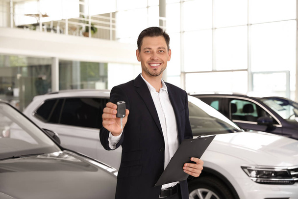 Salesman with clipboard and car key standing in salon - Photo, image