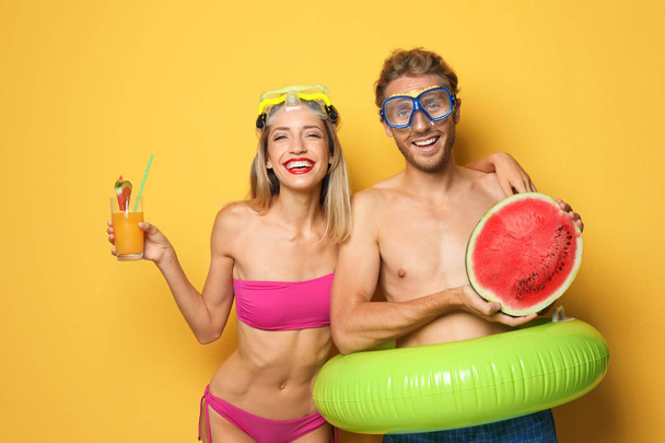 Happy young couple in beachwear with inflatable ring and cocktail on color background - Foto, Imagen