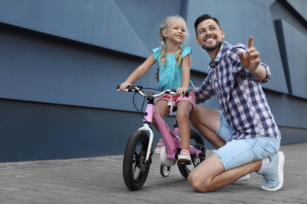 Father teaching son to ride bicycle on street - Zdjęcie, obraz