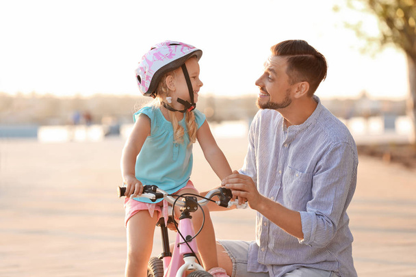 Father teaching daughter to ride bicycle on street - Fotoğraf, Görsel