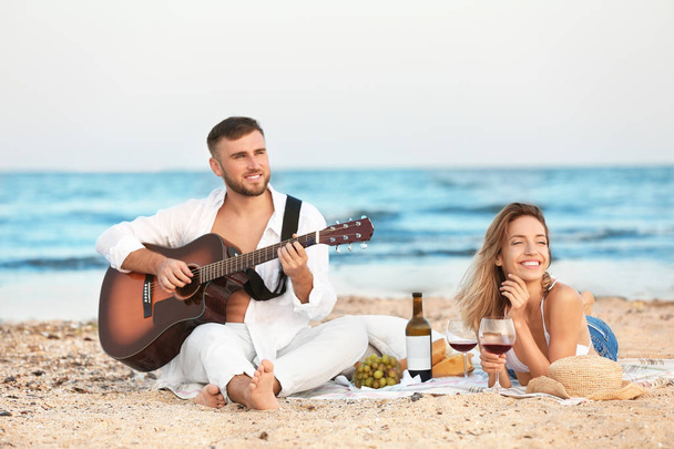 Young couple with guitar having romantic dinner on beach - Foto, imagen