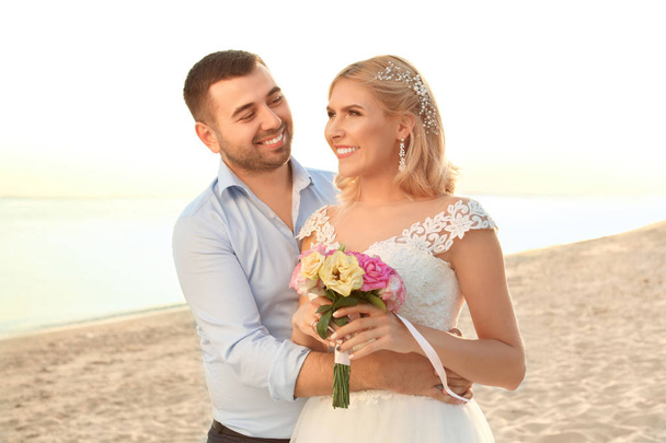 Pareja de bodas. Novia y novio abrazándose en la playa al atardecer
 - Foto, Imagen