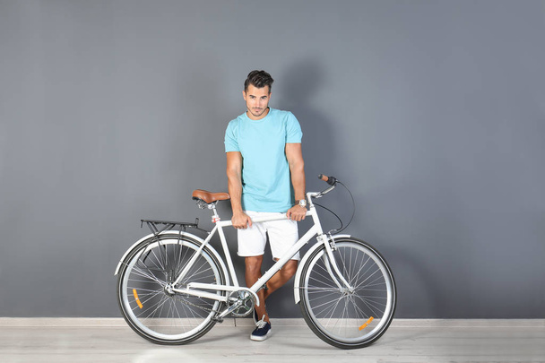 Handsome young hipster man with bicycle near color wall - 写真・画像