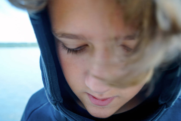Portré szomorú tizenéves fiú a folyó vagy tó partján. Aranyos fiú egy visel a fekete kapucnis kapucnis göndör hajjal. Közelről. Serdülő, tinédzser. - Fotó, kép