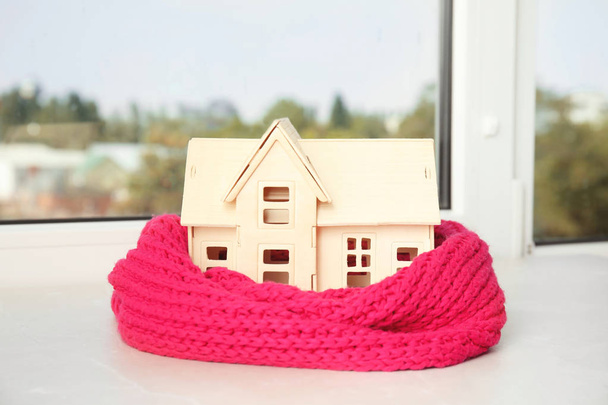 Huis model met gebreide sjaal op tafel tegen onscherpe achtergrond. Verwarming concept - Foto, afbeelding